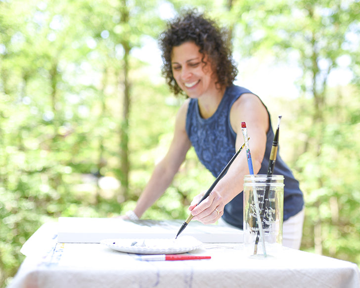 The designer and artist Kris Fiore smiling while painting outdoors